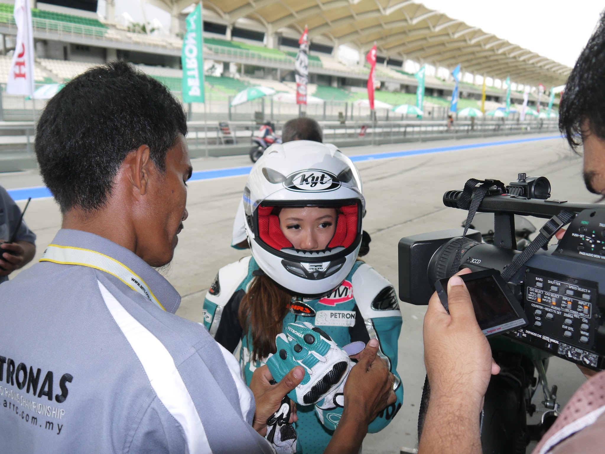 Louisa in motorcycle racing gear, surrounded by a camera crew at a race circuit